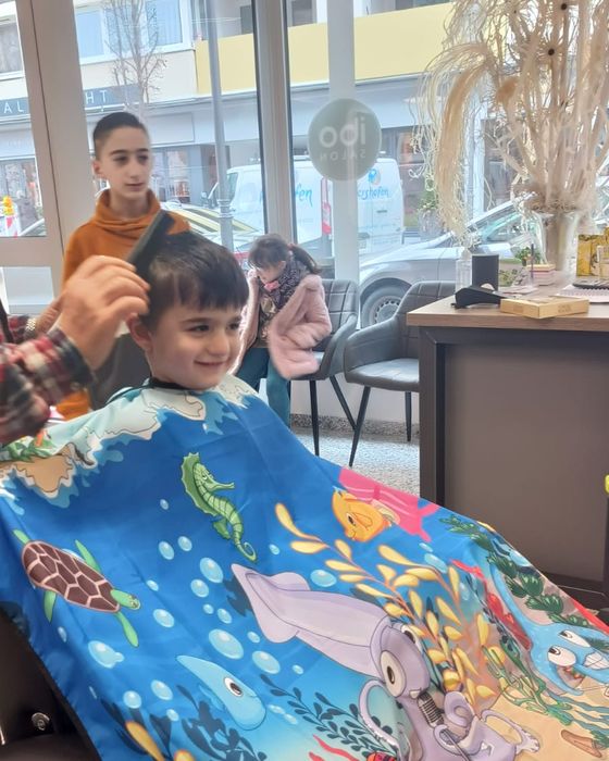 Kind auf dem Friseurstuhl, im Hintergrund der Salon